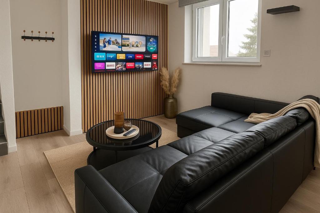 Magnifique Logement indépendant 5 min Colmar parking wifi في فينتزنهايم: غرفة معيشة مع أريكة جلدية سوداء وطاولة