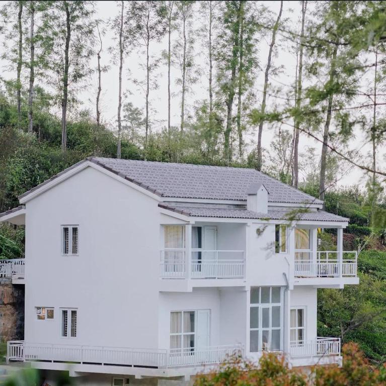 a white house with a balcony and trees at Prithivee Homestay in Kotagiri