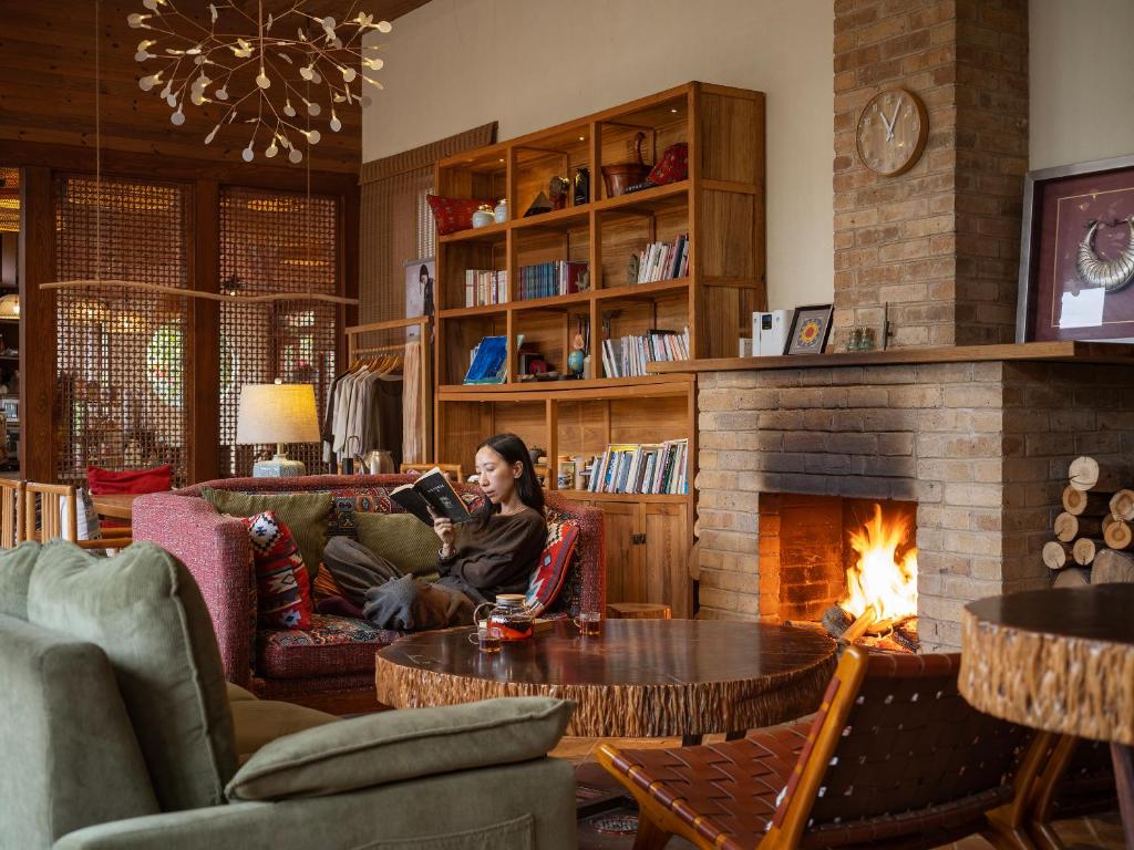 a woman sitting on a couch in a living room with a fireplace at Yangshuo The Apsara Lodge in Yangshuo