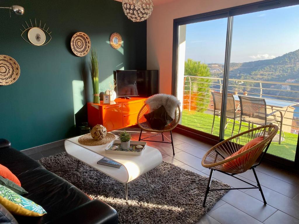 a living room with a couch and chairs and a large window at Résidence Costa Vermella, vue mer et montagne au calme in Cerbère