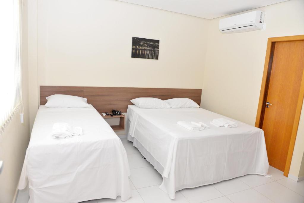 Habitación con 2 camas, sábanas blancas y mesa. en Cajueiro Hotel, en Floriano