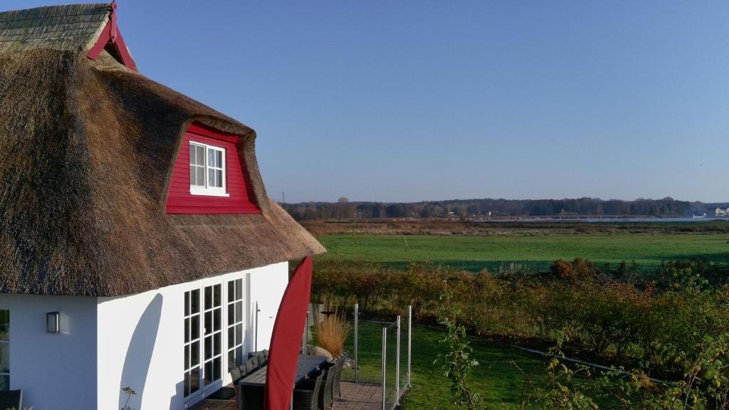 una casa con il tetto di paglia, una finestra rossa e un campo di Krügers Auszeit a Zinnowitz