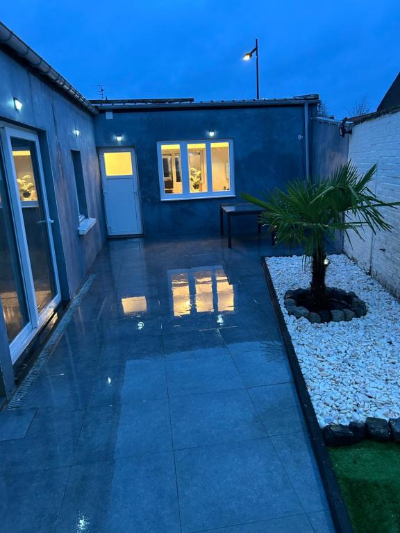 a patio with a blue building and a palm tree at Maison Relax Spa & tranquillité in Auberchicourt