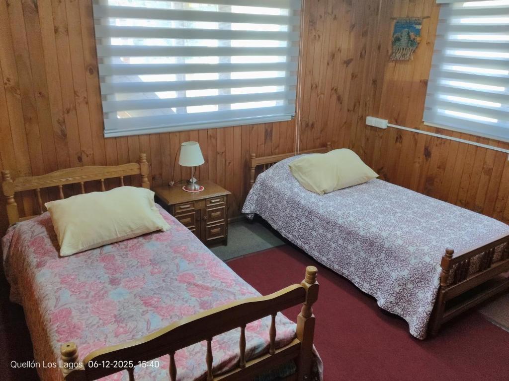 two beds in a room with wooden walls and windows at Hospedaje Mirador del Puerto in Quellón