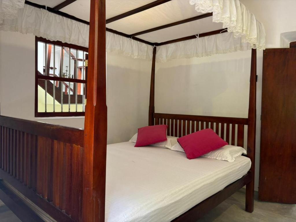 een slaapkamer met een hemelbed met rode kussens bij John's Homestay in Talpe