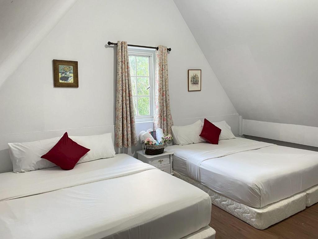 two beds in a room with white walls and red pillows at Chermonné House เฌอมอญ 