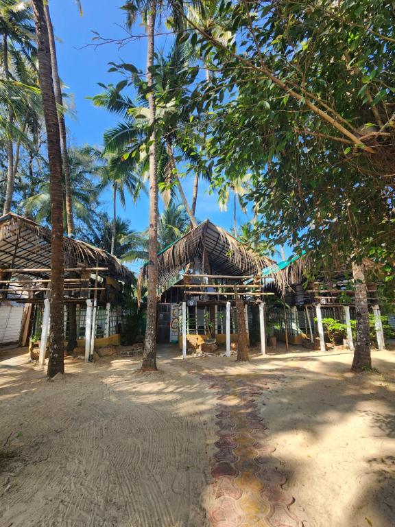 a building with a straw roof with palm trees at Cozy Nook Goa Palolem in Palolem
