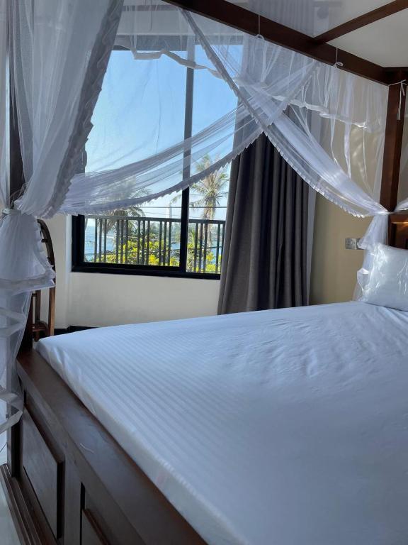 a bedroom with a white bed with a window at Dondra OceanLight Villa in Gandara East