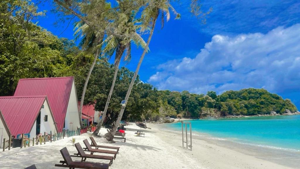 a beach with benches and a red building and the water at DEWATI ROOMSTAY B&B in Lang Tengah