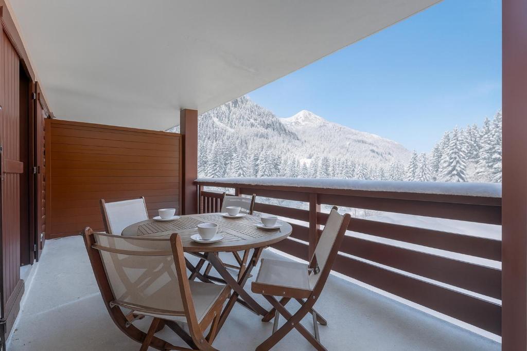 einen Tisch und Stühle auf einem Balkon mit schneebedeckten Bergen in der Unterkunft l'Ours Bleu C21 - Ski In Ski Out - Happy Rentals in Vallorcine