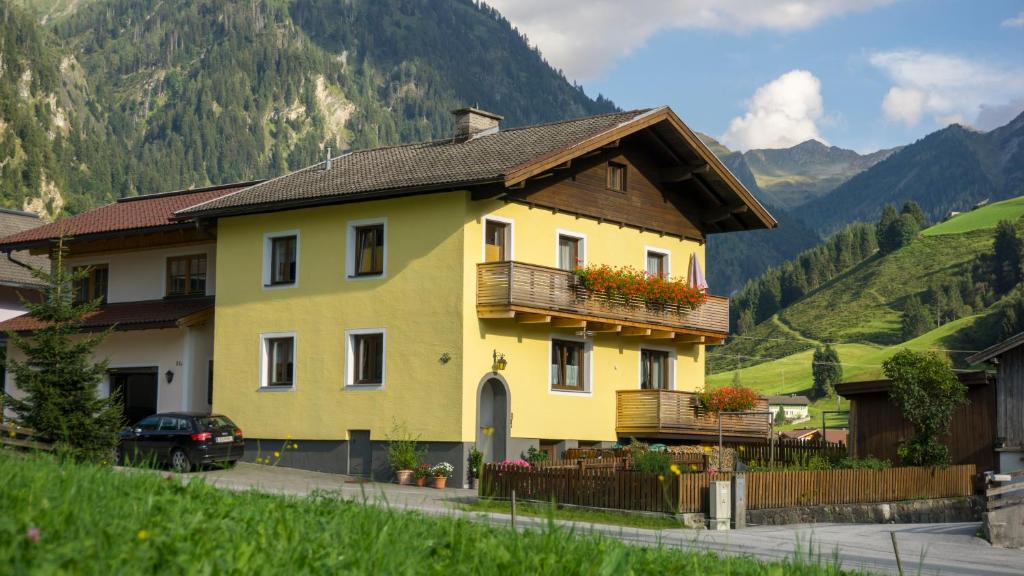 a yellow house with a balcony and mountains in the background at Haus Elisabeth in Hüttschlag
