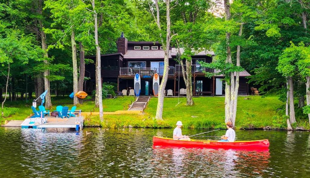 two people in a red boat on a lake with a house at Lakefront Hot Tub Canoes Game Room Wood FP in Gouldsboro