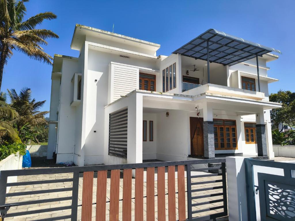 a white house with a fence and palm trees at The white luxury Homestay in Thekkady