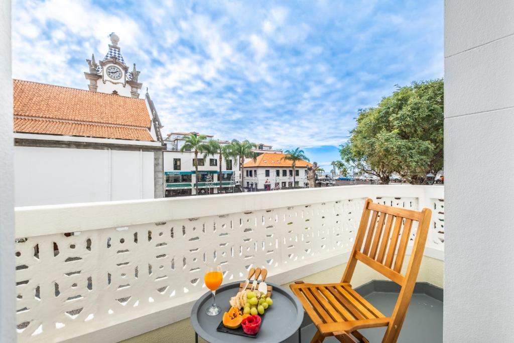 a table and a chair on a balcony with a clock tower at Reis by KAAMAH in Ribeira Brava