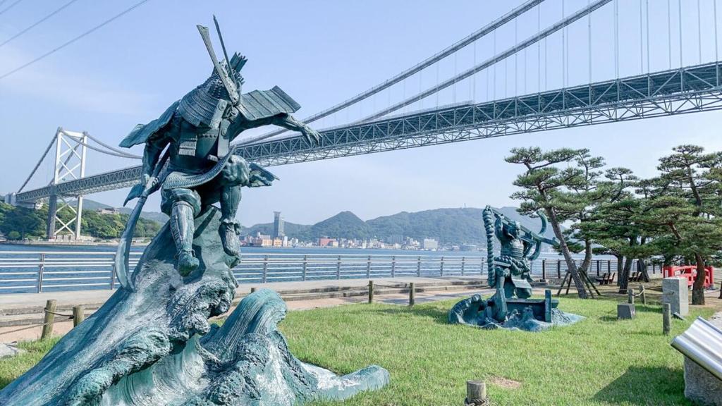 Una estatua de un hombre parado sobre un tronco junto a un puente. en インジホテル下関, en Shimonoseki