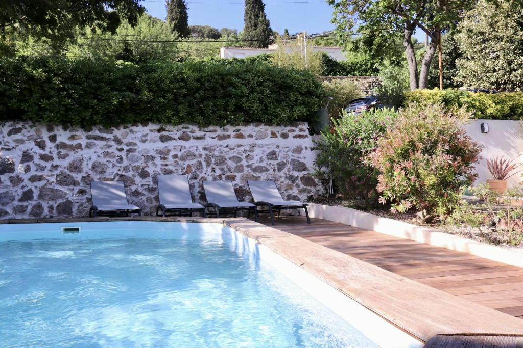 a swimming pool with chairs next to a stone wall at Chambre d'hôtes Les terrasses de Saint Clair in Sète