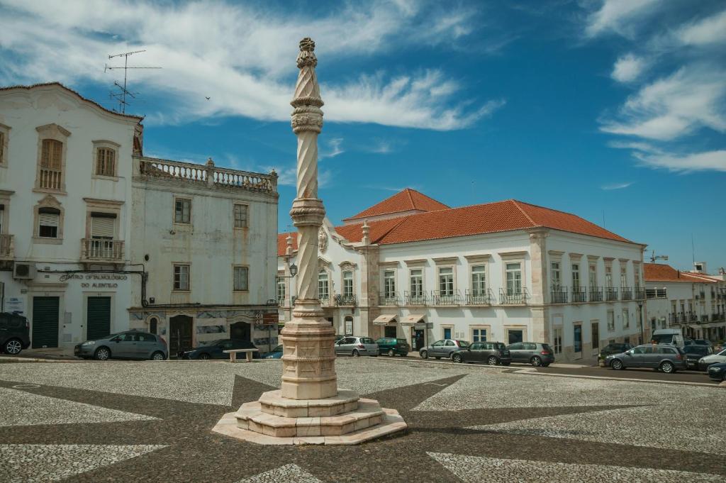 Una statua in mezzo a una strada con edifici di Casa Rainha Santa a Estremoz