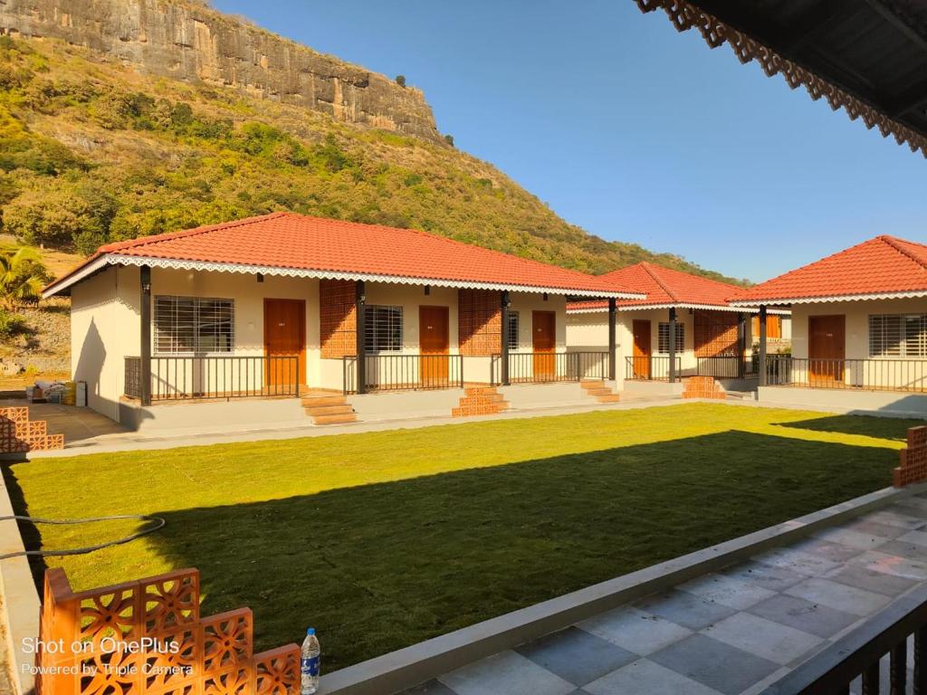 een huis met een groen gazon voor een heuvel bij Shivjanmabhumi Resort in Junnar