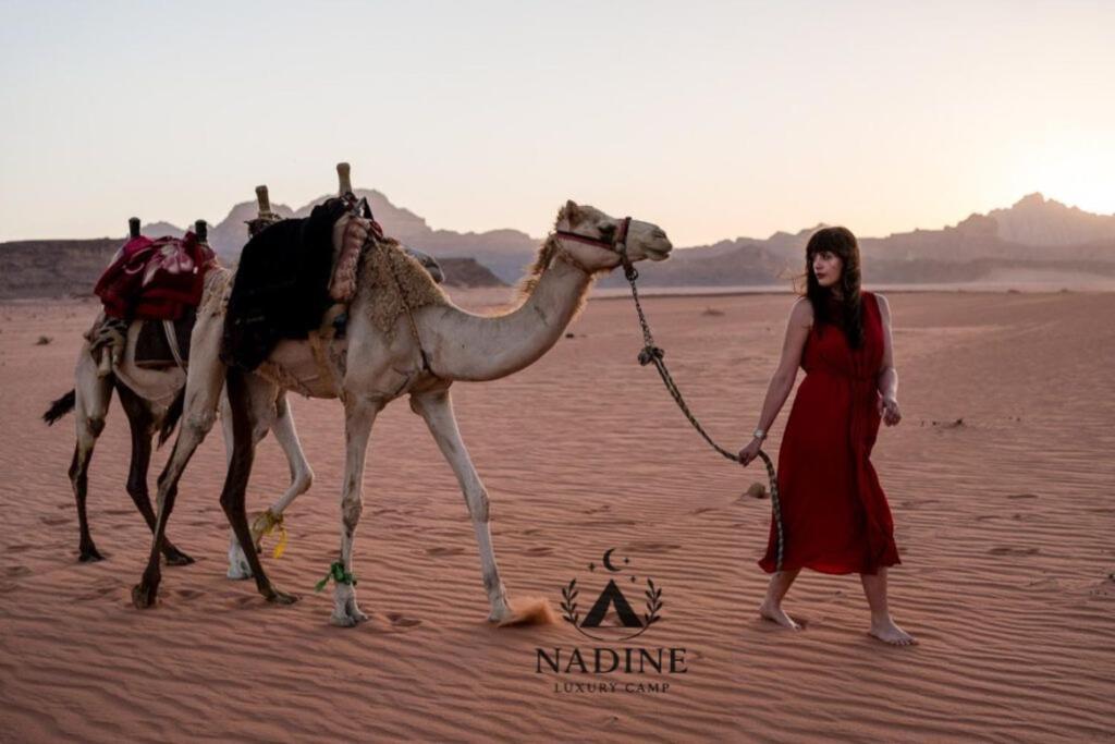 een vrouw in een rode jurk met een kameel in de woestijn bij Nadine Luxury Camp in Wadi Rum