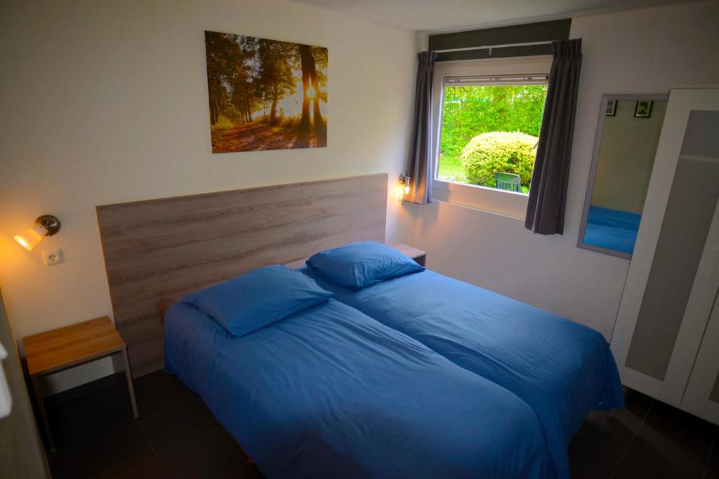 ein Schlafzimmer mit einem Bett mit blauen Laken und einem Fenster in der Unterkunft Bungalow 21 - Nelderhut in Simpelveld