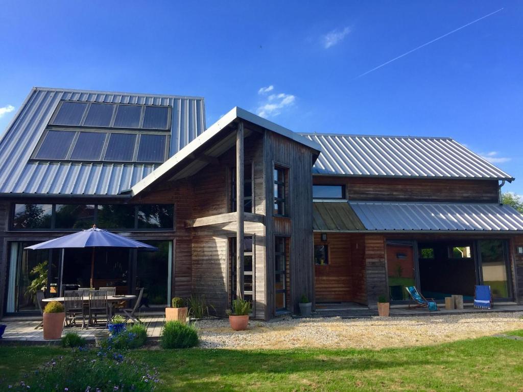 ein Haus mit Metalldach, auf dem ein Tisch und ein Sonnenschirm stehen. in der Unterkunft La Verrière - maison écologique normande 