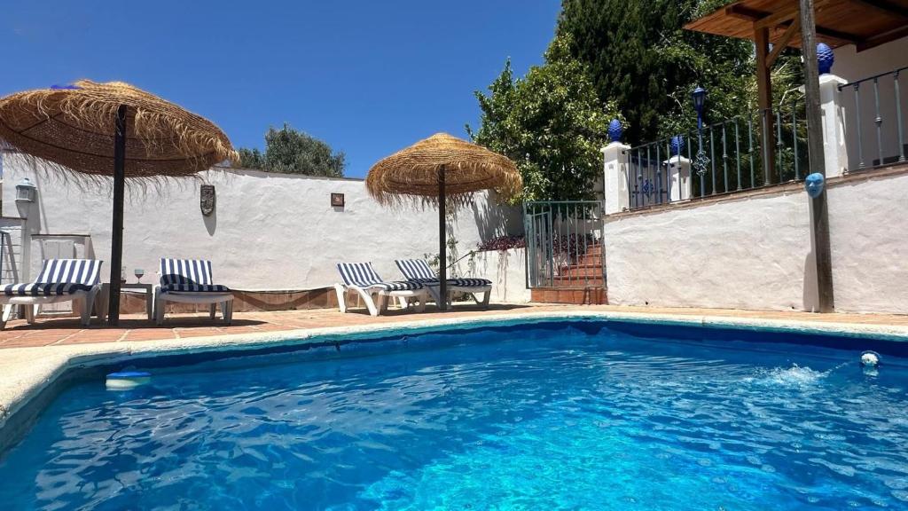 una piscina con dos sillas y dos sombrillas en Villa vistas al lago with private pool, en Viñuela
