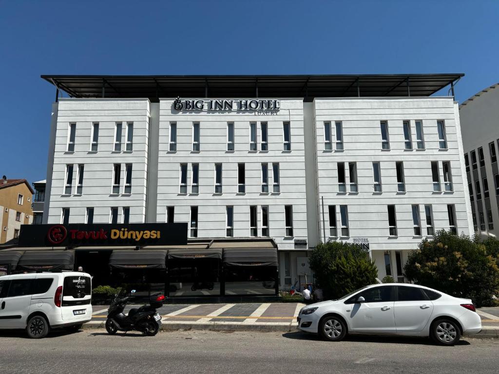 due auto parcheggiate di fronte a un edificio bianco di Big Inn Luxury Hotel a Biga