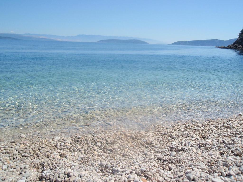 a beach with rocks and the clear blue water at Rooms Kučić in Cres