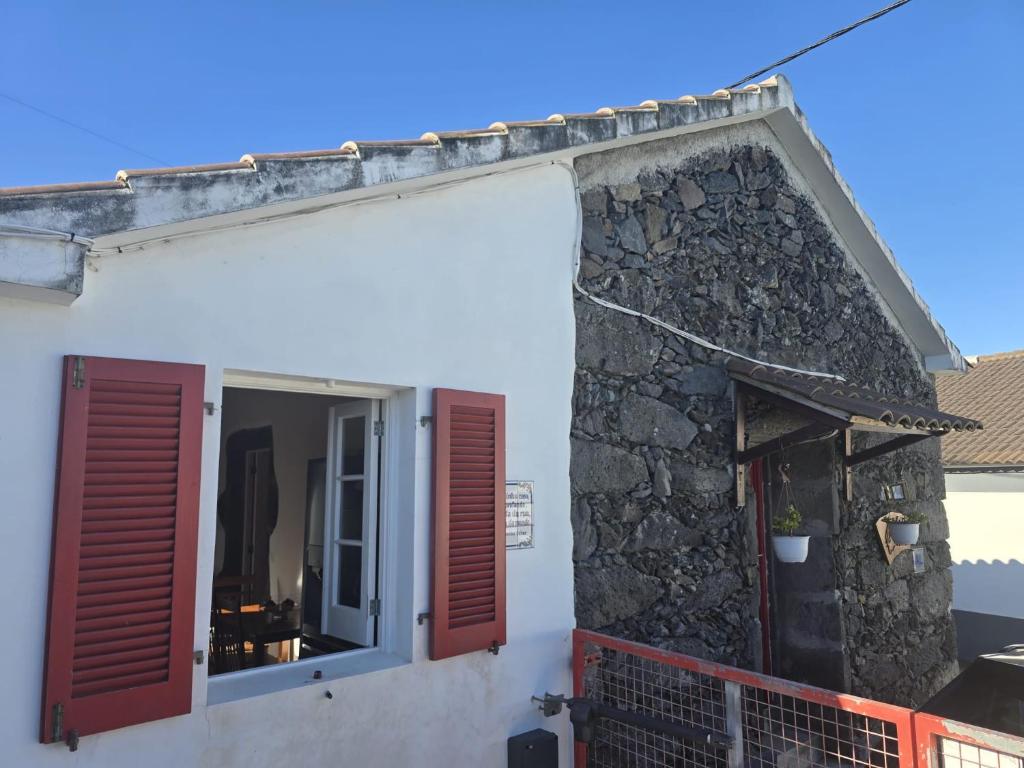 a building with red shutters and a stone wall at Recanto Vital in Achadinha