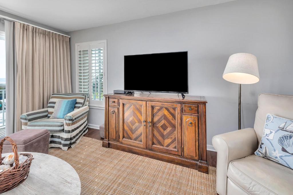 a living room with a flat screen tv and a chair at Beach Club #211 in East End