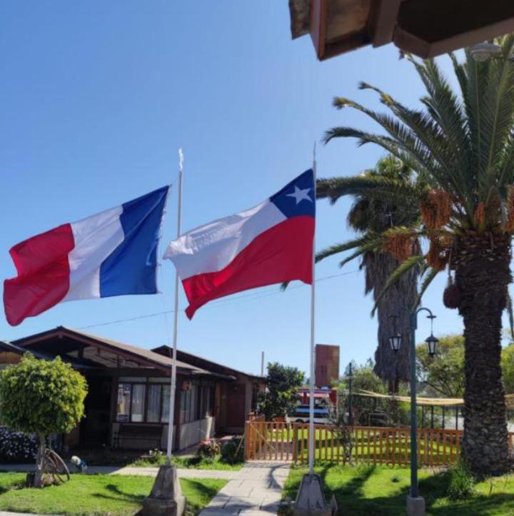 two flags in front of a house with a palm tree at Las Cabañas del Francés in Vallenar