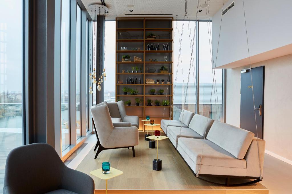 a living room with a couch and two chairs and windows at Hotel Indigo Berlin - East Side Gallery in Berlin
