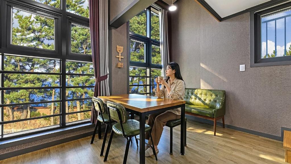 a woman sitting at a table in a room with windows at Samcheok Lamer Pension in Samcheok