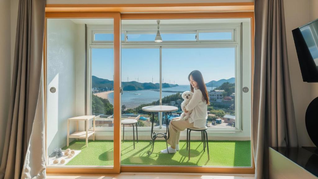 Una mujer sentada en un taburete en una ventana con un osito de peluche. en Yeongheungdo noeul&bada pension, en Incheon