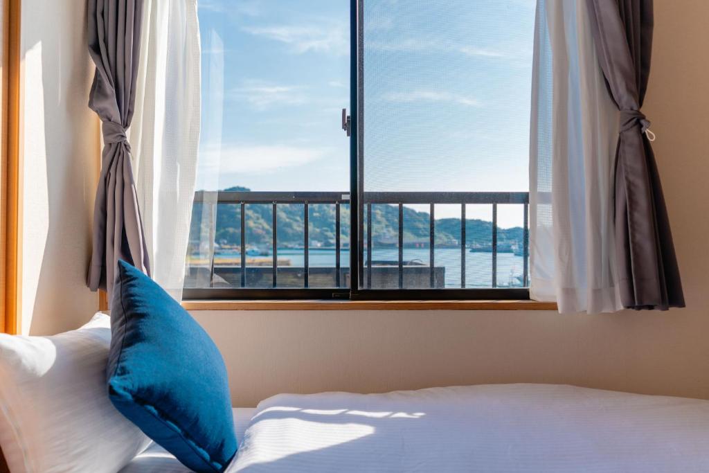 a bed with a blue pillow in front of a window at Good Stay Apartment in Nichinan