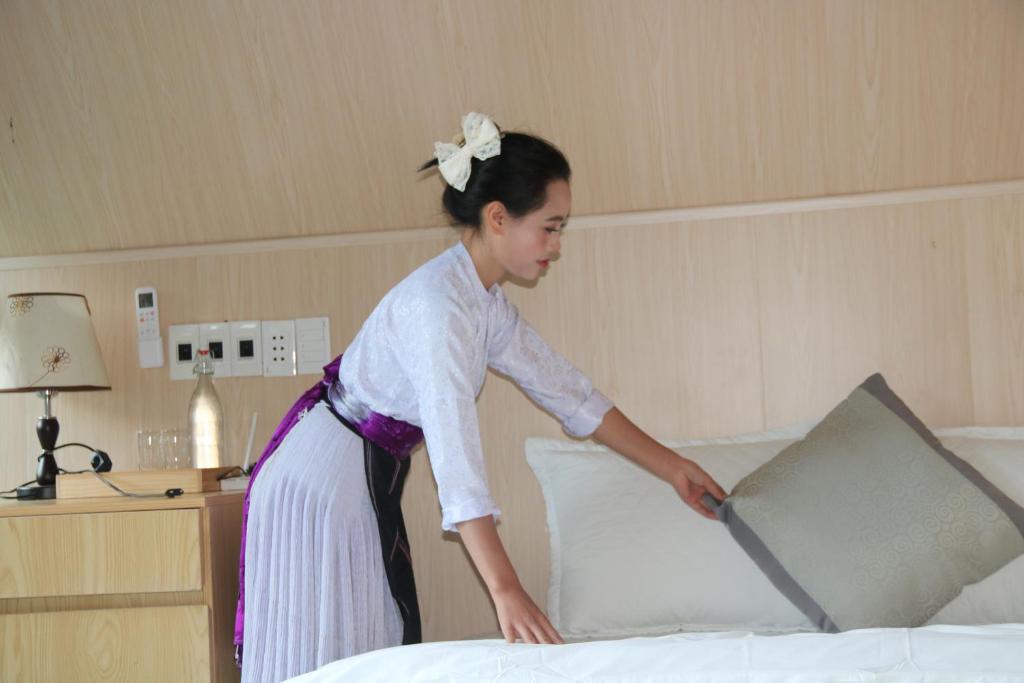 eine Frau legt ein Kissen auf ein Bett in der Unterkunft Pavi Lodge in Mèo Vạc