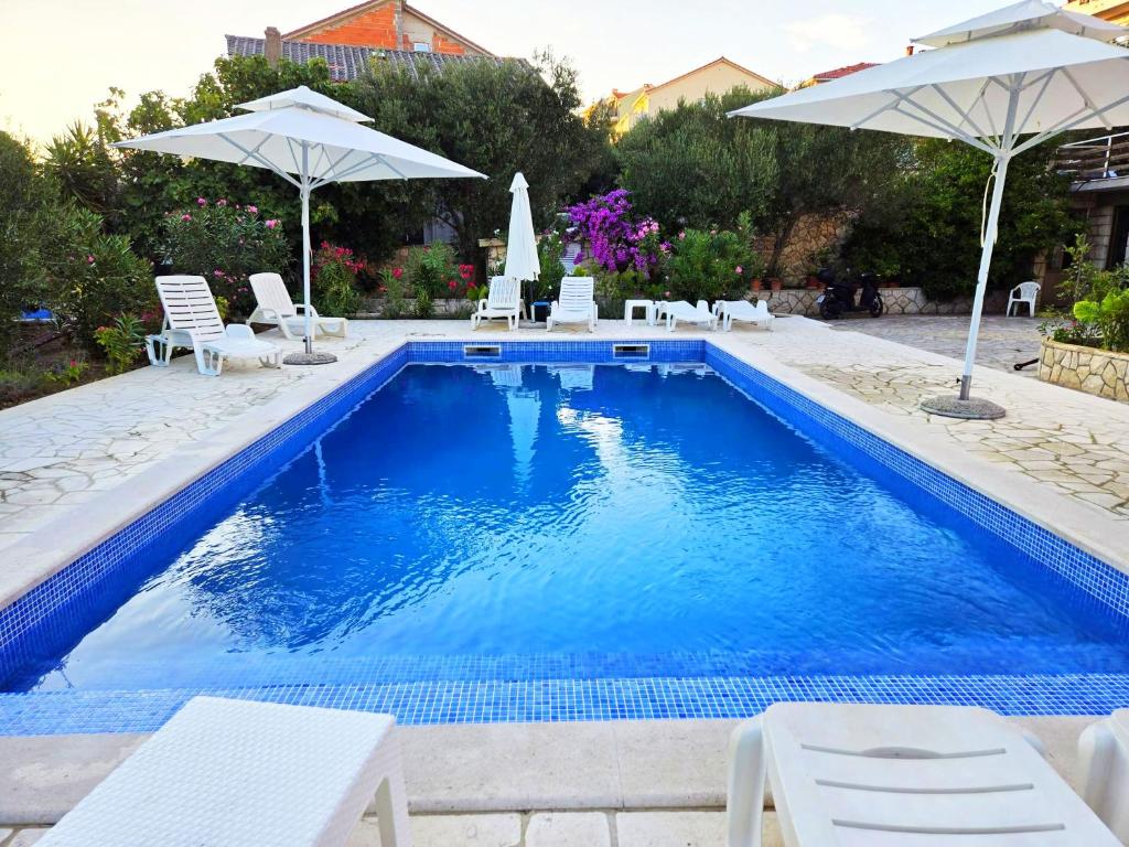 uma piscina com cadeiras brancas e guarda-sóis em Visy in Center Novalja with Pool em Novalja