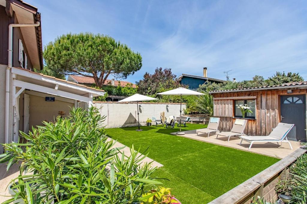 einen Hinterhof mit einer Liegewiese mit Stühlen und Sonnenschirmen in der Unterkunft Villa Rose des Sables, 100m de la Plage et Centre in Lège-Cap-Ferret