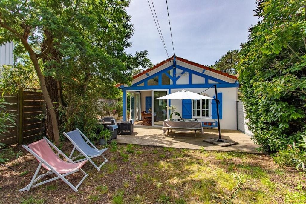 ein blau-weißes Haus mit Stühlen und einem Sonnenschirm in der Unterkunft Villa 3 chambres dans le centre du Cap Ferret in Lège-Cap-Ferret