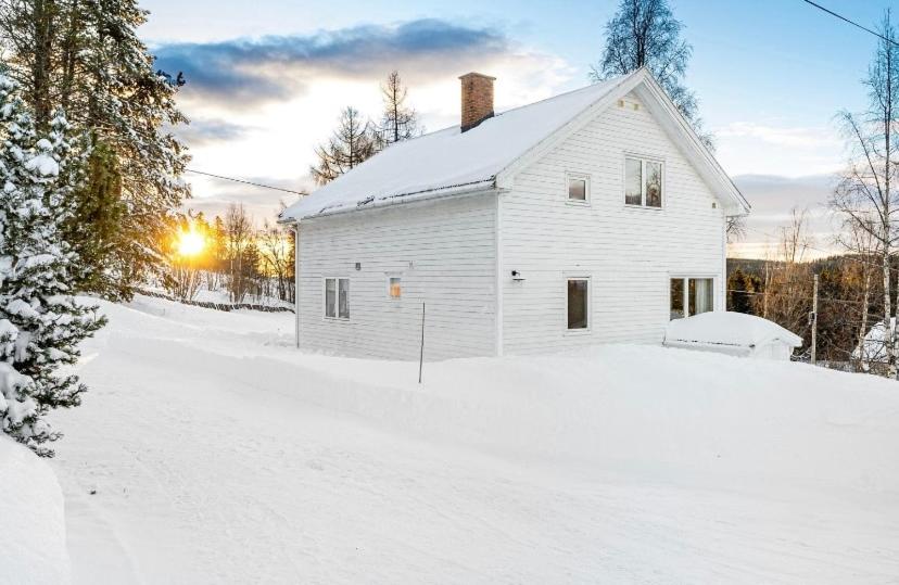 Ein weißes Haus im Schnee mit der Sonne dahinter. in der Unterkunft A Cozy Nordic Home in Ålset