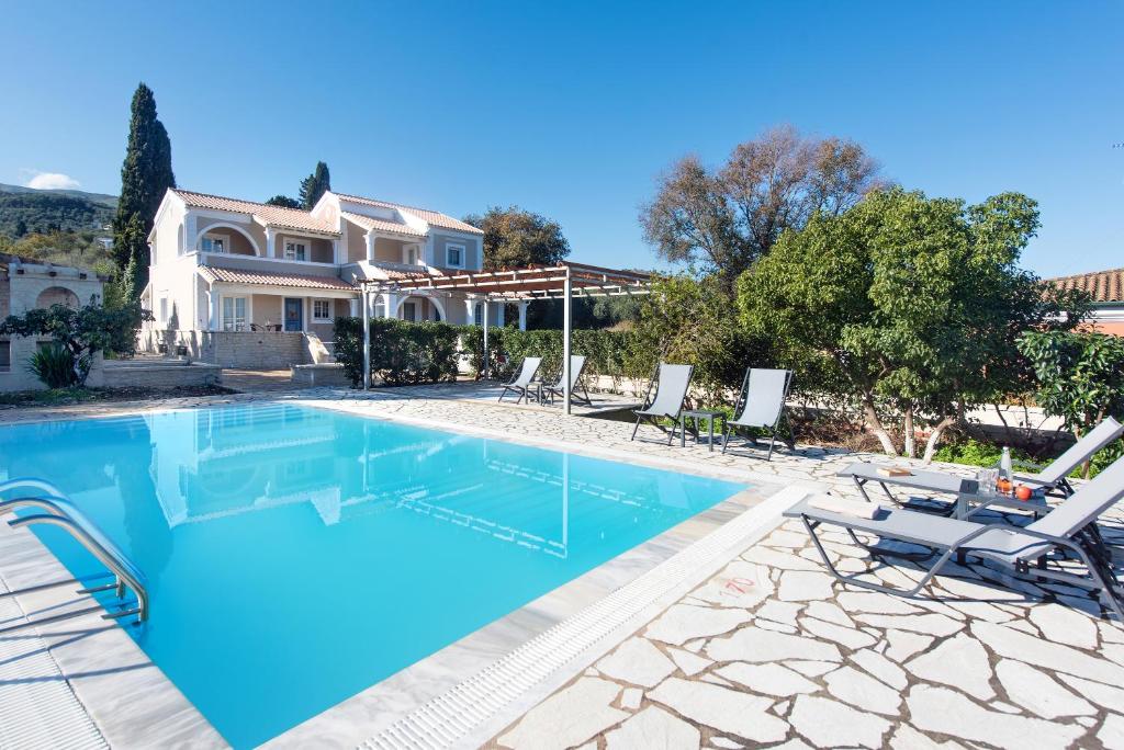 a swimming pool with chairs and a house at Nancy Luxury Suites in Kassiopi