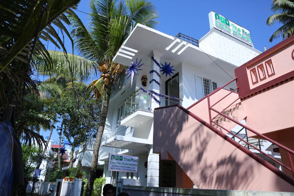 a white building with palm trees in front of it at The Pod Cochin Homestay in Cochin