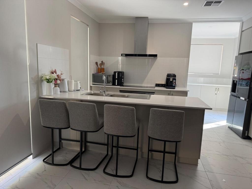 a kitchen with a counter with four bar stools at Wellard Nest- Perth- Newly built house, walk to the shops and train station- Close to Rockingham and motorplex in Wellard