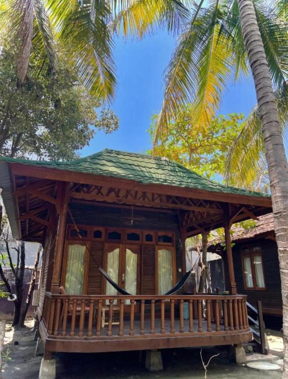 a cabin with a hammock in front of a palm tree at Bronze Bungalow in Gili Meno