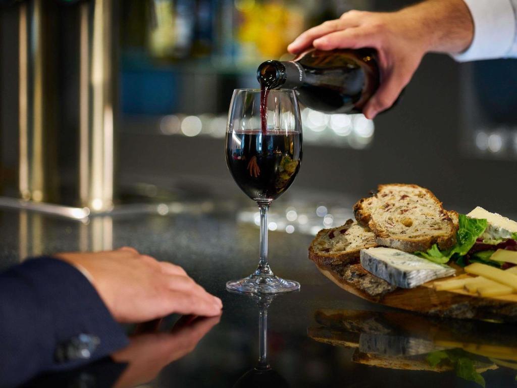 una persona que vierte vino tinto en una copa de vino en Novotel Massy Palaiseau, en Palaiseau