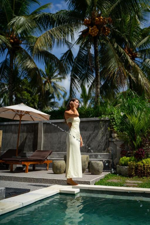 a woman in a white dress standing next to a swimming pool at Grita Apsari Lodge Ubud by Lefanna in Tegalalang