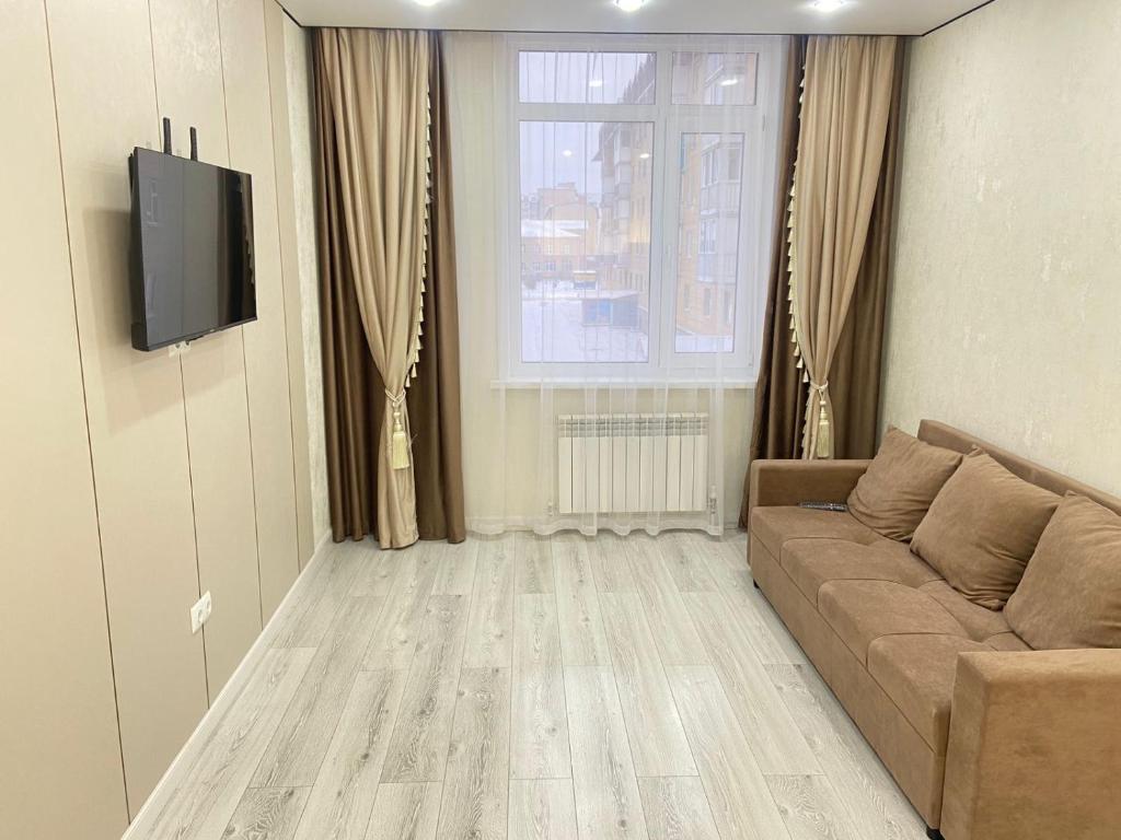 een woonkamer met een bank en een televisie bij Кокшебель Жк in Astana
