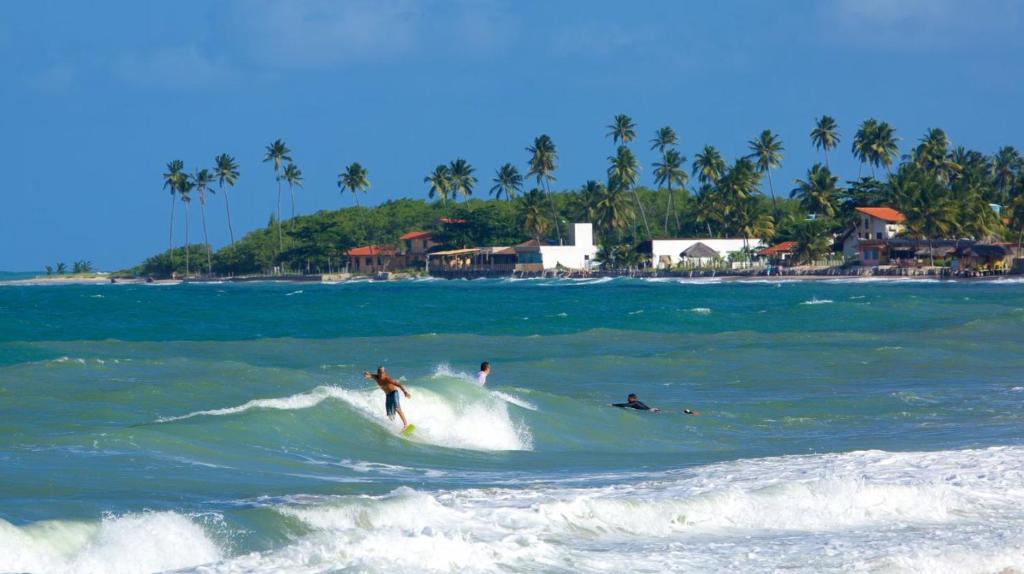 Un gruppo di persone che cavalca un'onda nell'oceano di Quarto Duplo com Ar e Banheiro Privativo a poucos metros do mar a Porto De Galinhas