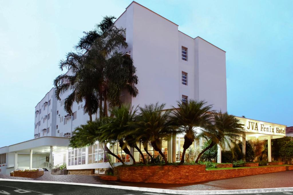 a white building with palm trees in front of it at JVA Fenix Hotel in Uberlândia