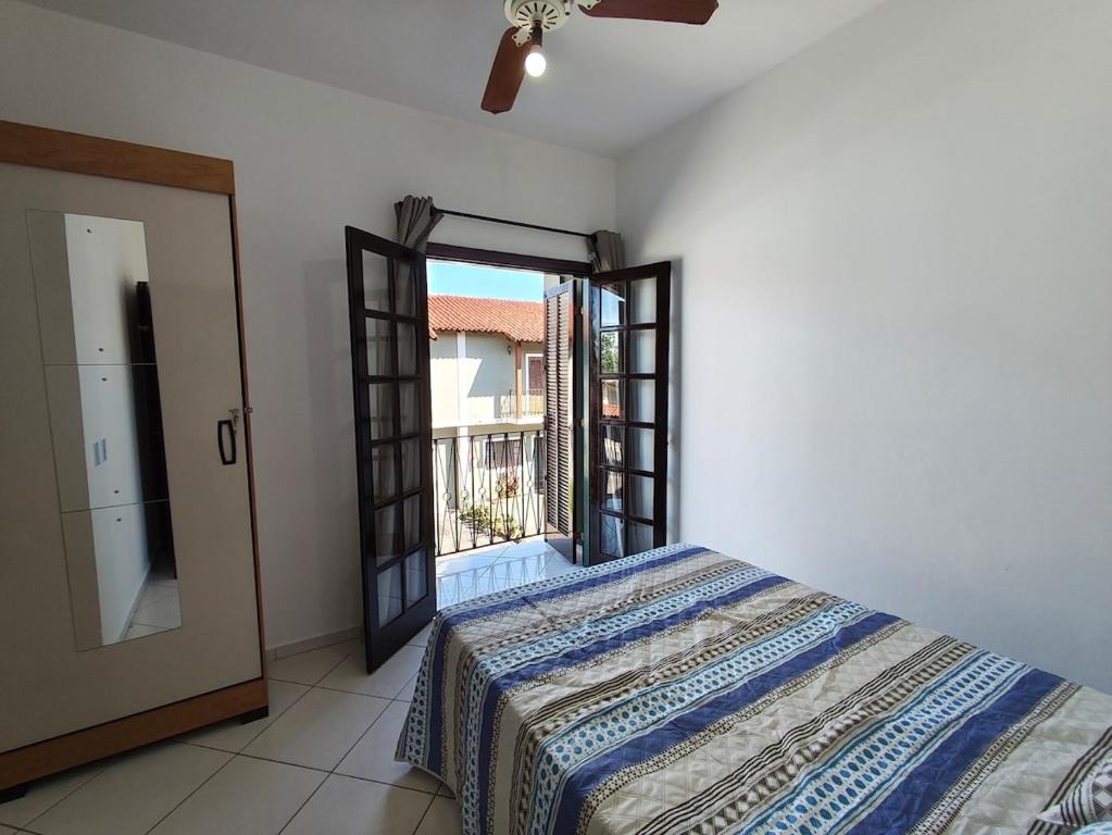 een slaapkamer met een bed en een deur naar een balkon bij Casa em condomínio no centro de Bertioga in Bertioga